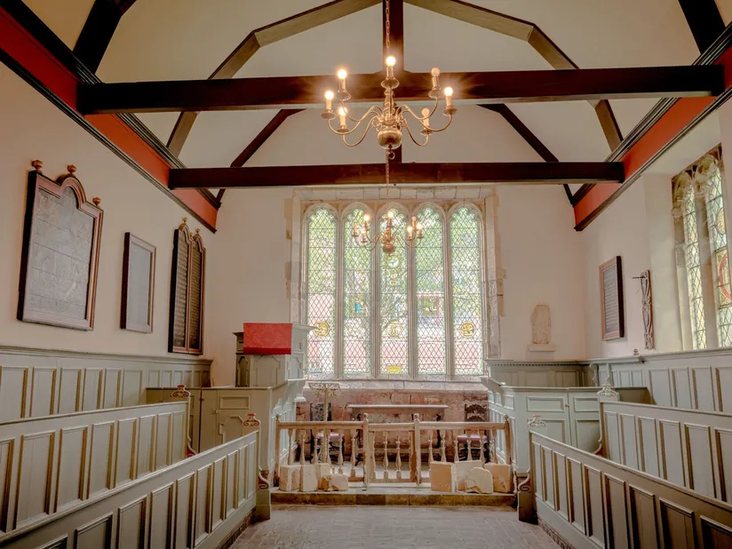 A warm chapel interior with red beams and a stained glass window