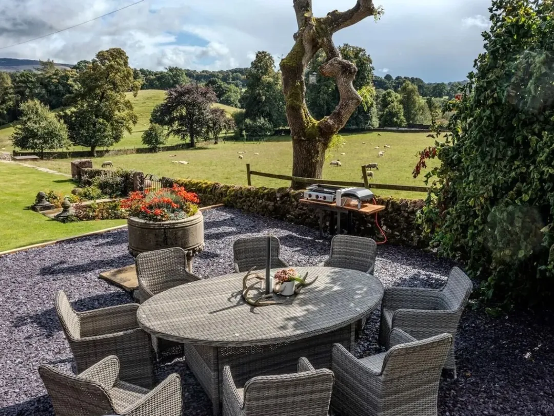 The stone patio with an outdoor dining table and chairs overlooking the fields
