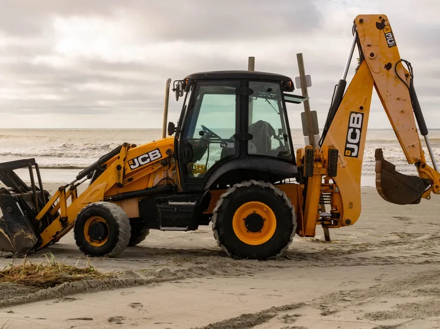 A JCB backhoe parked on the sandy shores of