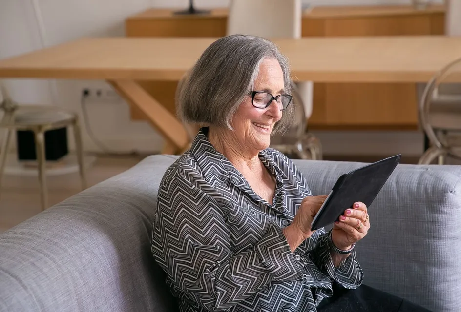 An older resident smiling as she reads her parish council website on a tablet at home
