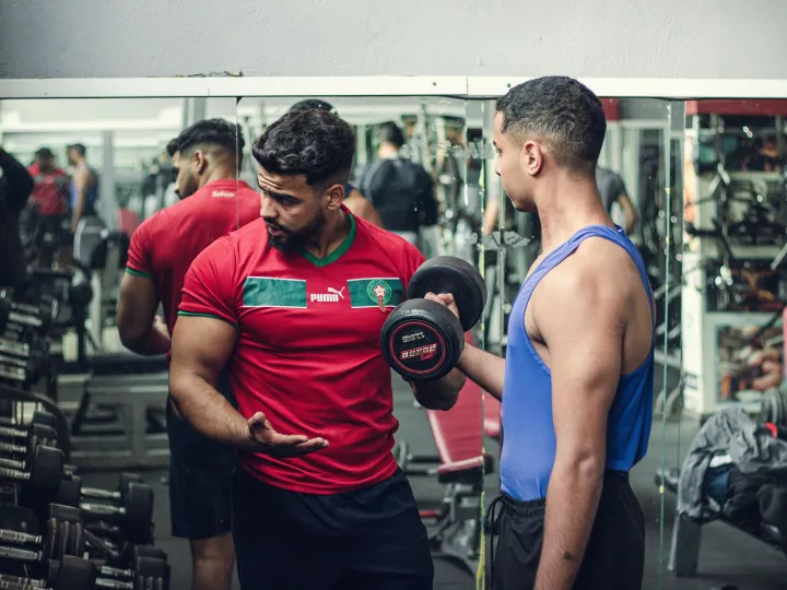 A personal trainer coaching a client lifting dumbbells in a gym