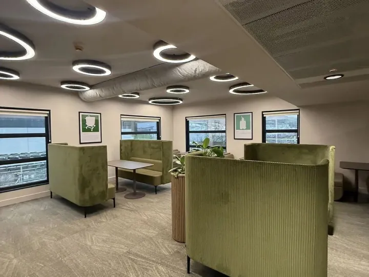 Breakout area with olive green high-backed booth seating, ring ceiling lights and framed prints