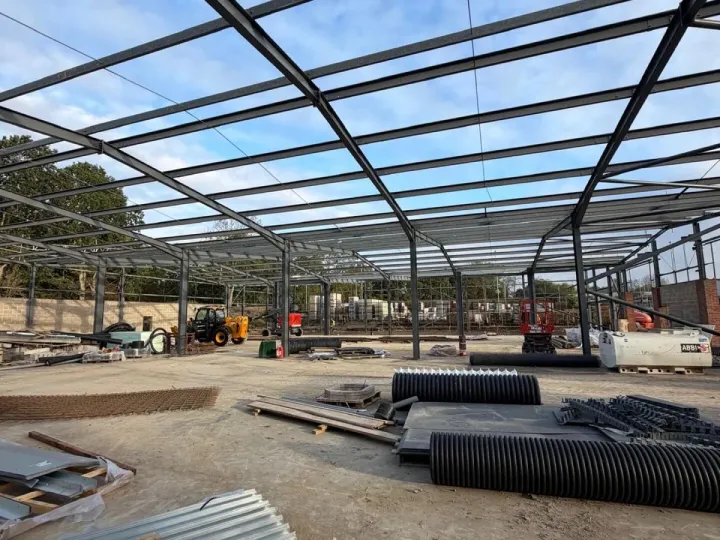 Dark painted steel portal frame against a blue sky, with roof sheets and drainage pipe on the slab below