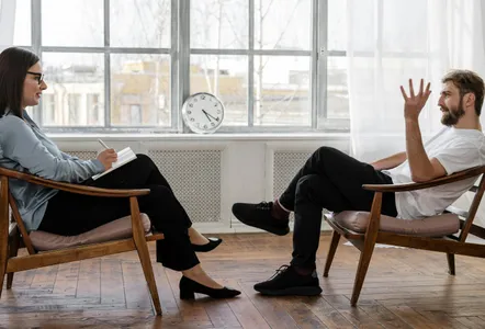 Person in Black Pants and Black Shoes Sitting on Brown Wooden Chair