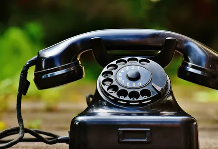 Close-up of a classic black rotary phone outdoors with a blurred green background.