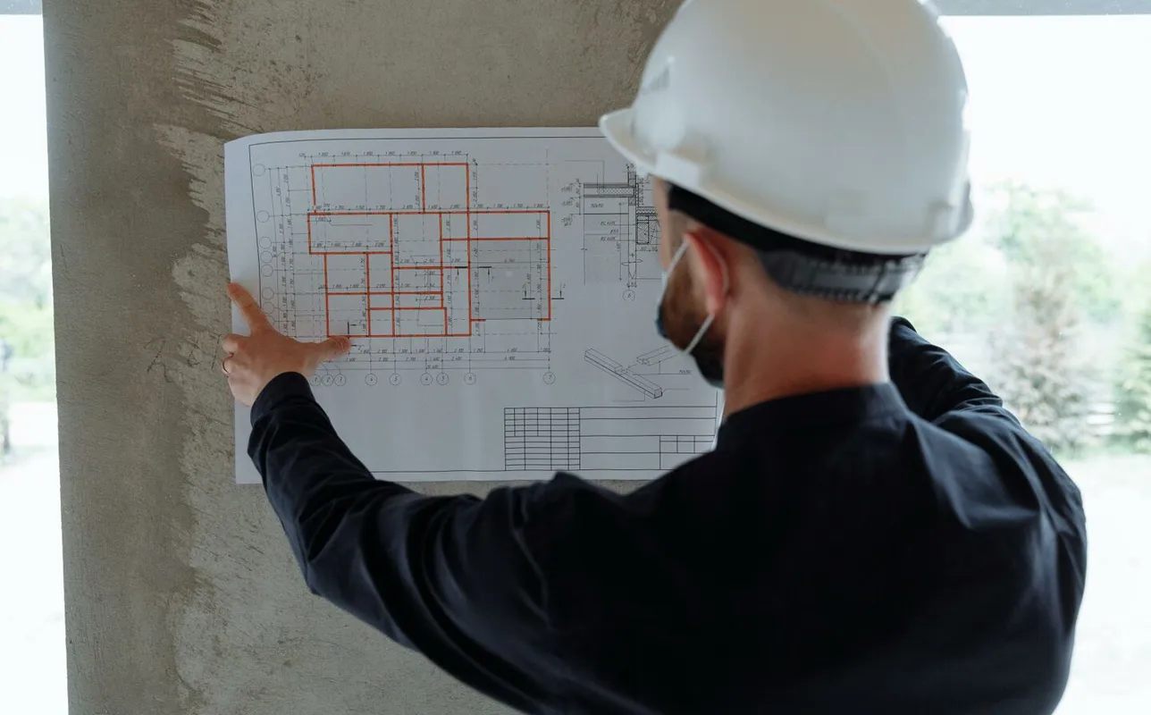 Engineer in hardhat reviewing architectural floor plans at construction site.