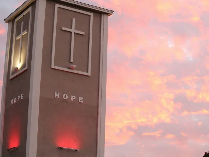 Illuminated church tower with crosses against a vibrant sunset sky.