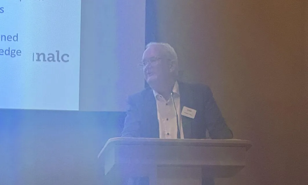 A speaker beside a screen showing a NALC presentation slide