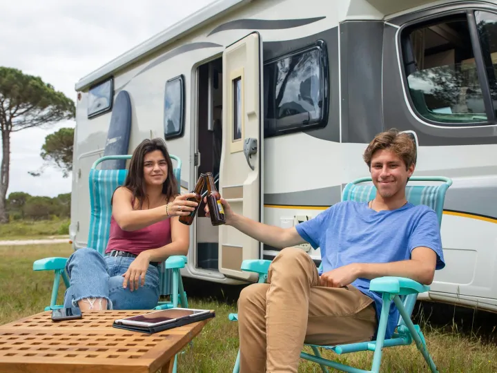 Happy couple clinking beer bottles outside camper