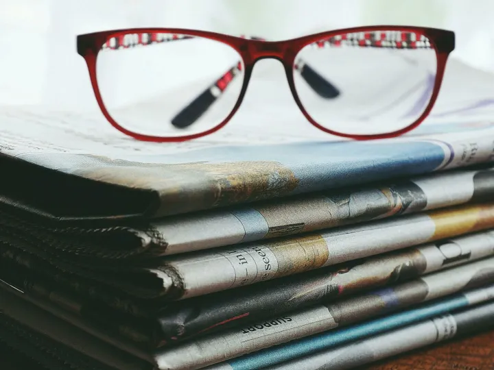 Red eyeglasses resting on a stack of newspapers symbolize reading and information.