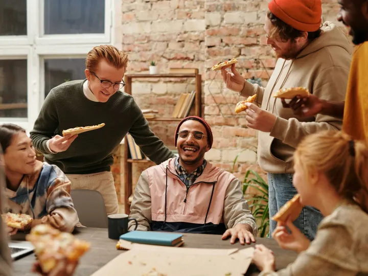 A joyful group of diverse friends enjoying pizza together in a cozy indoor setting.