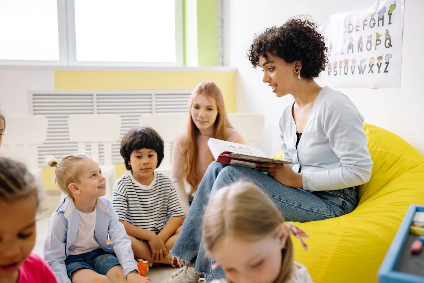 Nursery practitioner reading a story to a group of preschool children in a bright playroom
