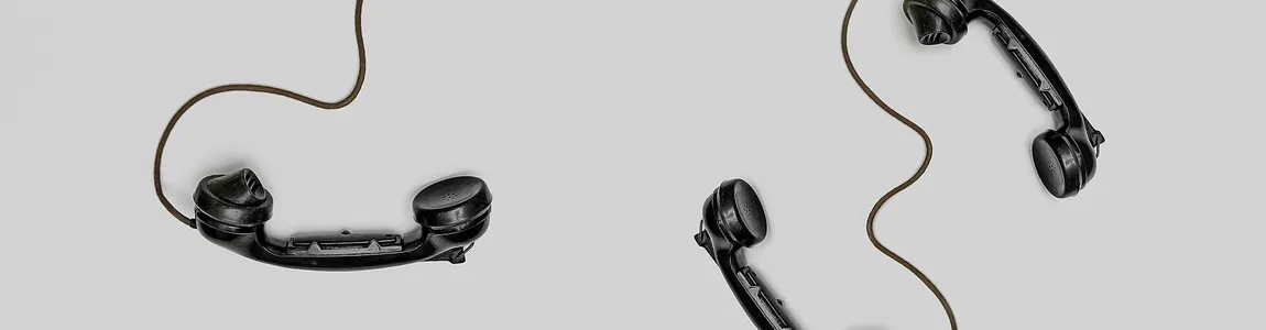 Two vintage black telephone handsets connected by cords on gray background.