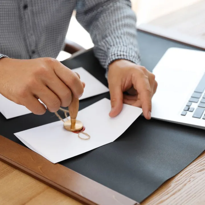 Hands pressing a wax seal onto a document at a desk