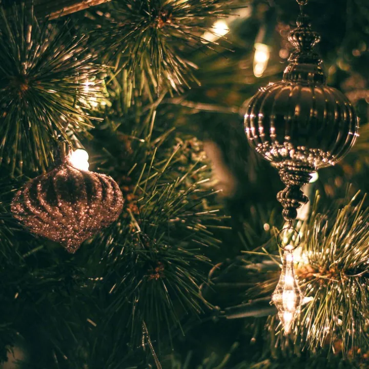 Close-up of sparkling Christmas ornaments hanging on a decorated tree with warm lights.
