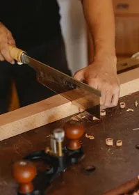 Carpenter cutting a length of timber with a hand saw at a workbench