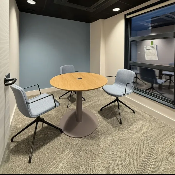 Small meeting room with a round oak table, blue chairs and a blue-grey painted feature wall