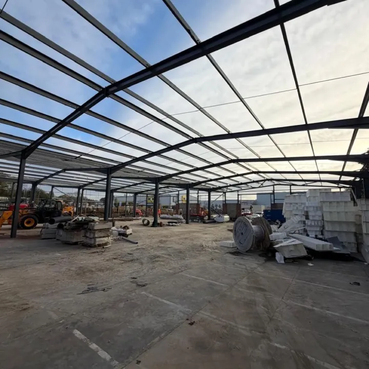 Dark painted steel portal frame of a large building under construction, with materials stacked on the slab