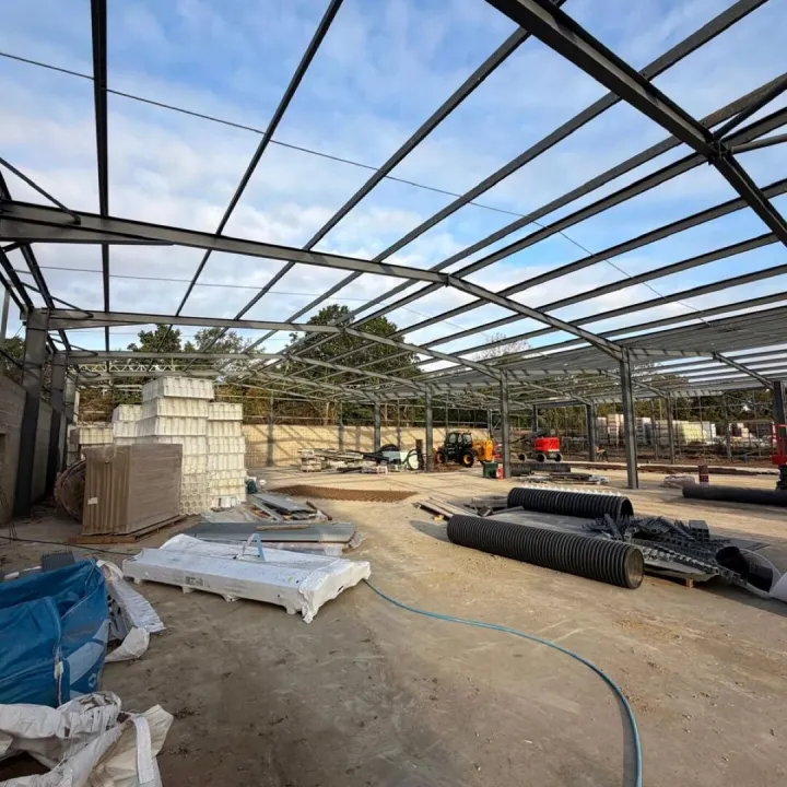 Interior of a dark steel portal frame building under construction, with crates and pallets on the slab