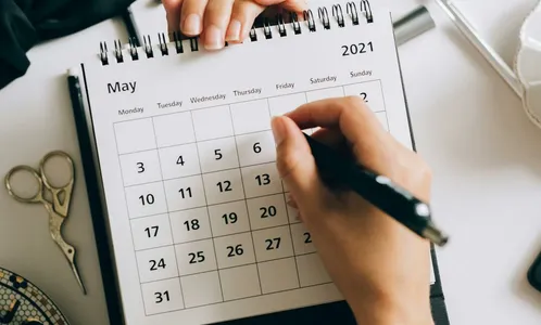Top view of hands using a planner with coffee and accessories, focused on May 2021 calendar.