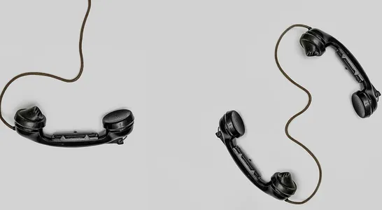 Two vintage black telephone handsets connected by cords on gray background.