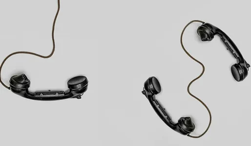 Two vintage black telephone handsets connected by cords on gray background.