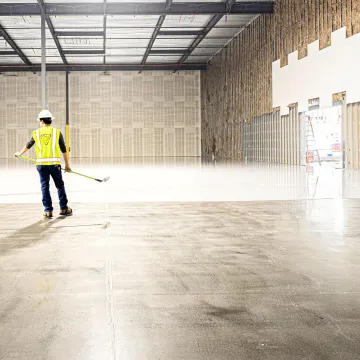 Worker in hi-vis jacket sweeping a warehouse floor