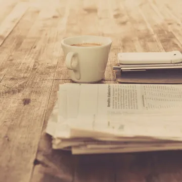 A warm vintage morning setup with coffee, newspaper, and smartphone on wooden table.