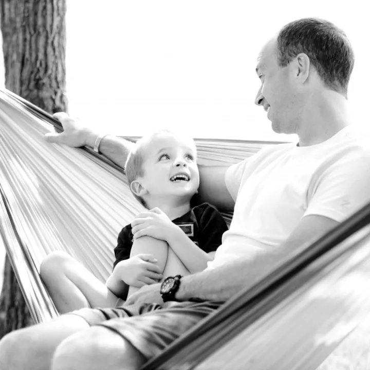Grayscale Photo of Man and Child Sitting on Hammock