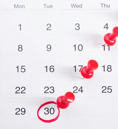 Close-up of a calendar with red push pins marking
