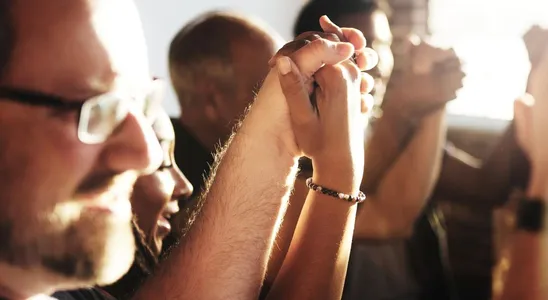 Group of people holding hands in a sunlit room symbolizing u