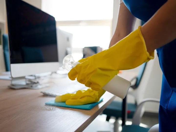 Gloved hand spraying and wiping down an office desk