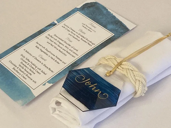 Hand lettered wedding menu card with a navy watercolour border and gold cord tie