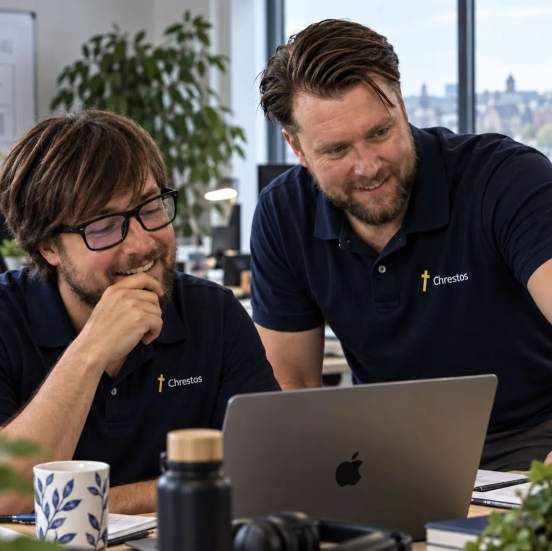 John and Toby from the Chrestos team, in Chrestos polo shirts, smiling at a laptop
