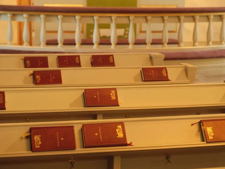 Red hymn books resting in the book racks of a chapel pew