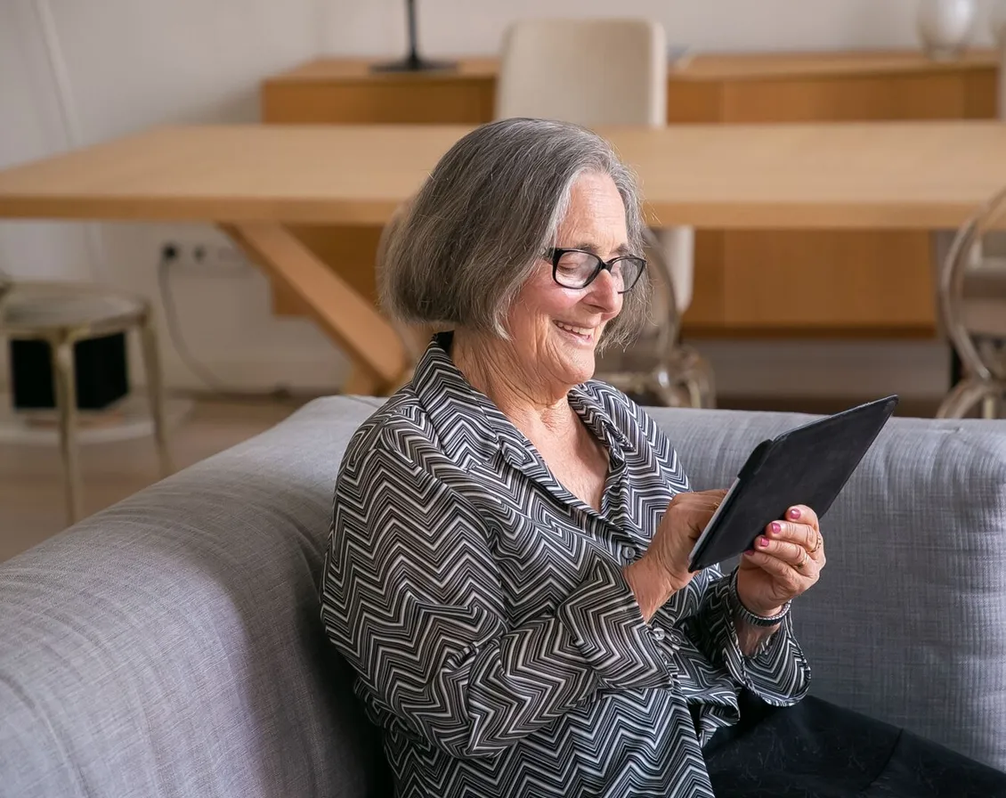 An older woman smiling as she reads a website on a tablet at home