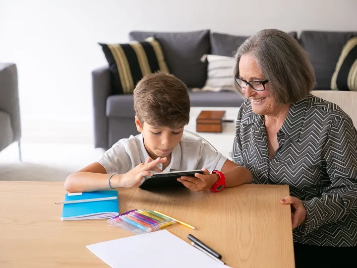 Grandparent helping a child use a tablet at a living-room table