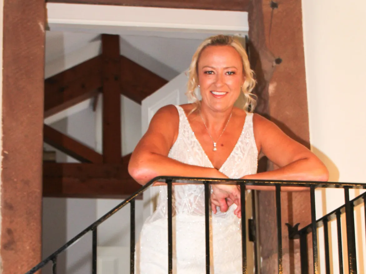 A bride smiling from the timber-framed staircase landing