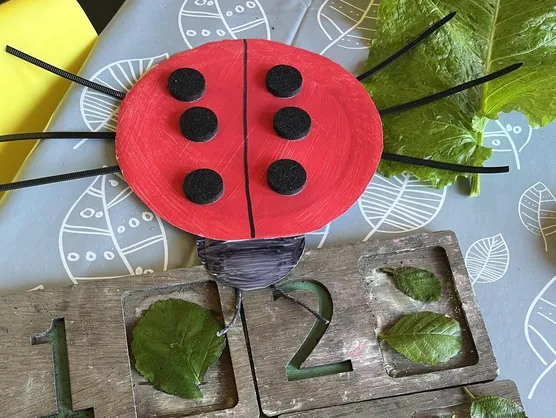 Wooden number blocks one to four filled with leaves beside a painted ladybird