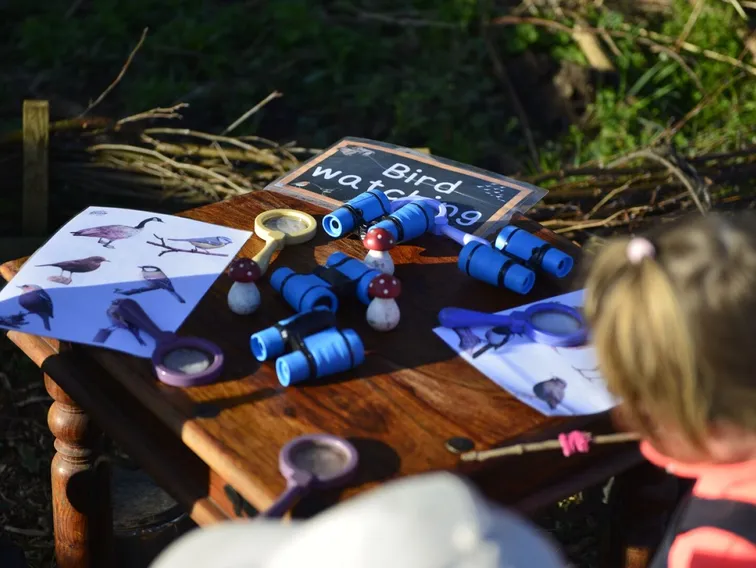 A bird watching table set out with toy binoculars, magnifying glasses and bird picture cards