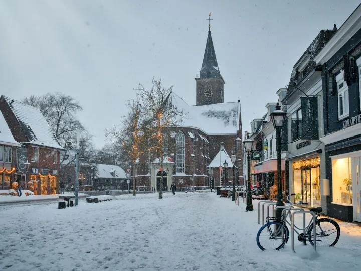 A snow-covered church and street with festive lights in winter