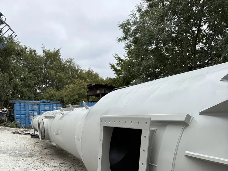 Primed grey steel chimney section with a large bolted square access opening, lying on gravel outdoors
