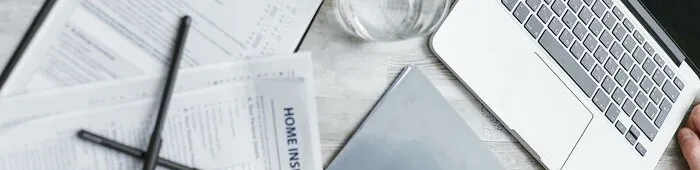 Person Writing on White Paper Beside Clear Glass Mug and Silver Macbook