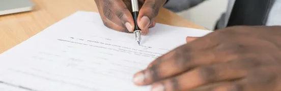 Person Holding Gray Twist Pen and White Printer Paper on Brown Wooden Table
