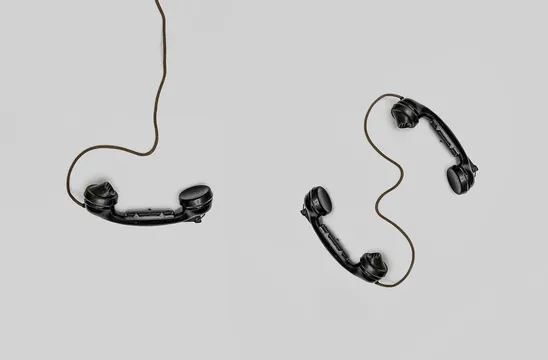 Two vintage black telephone handsets connected by cords on gray background.