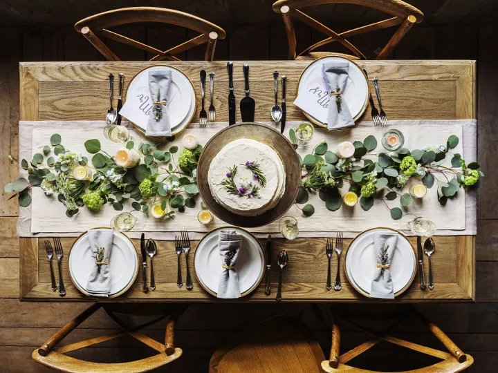 A long dining table laid for a private dinner, dressed with eucalyptus and white flowers