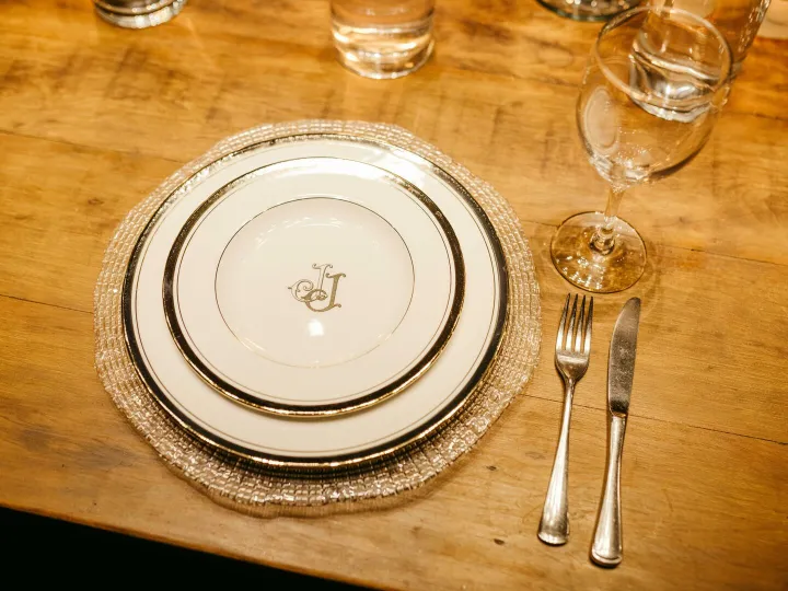 Luxurious dinner setting with monogrammed plates, cutlery, and glassware on a wooden table.