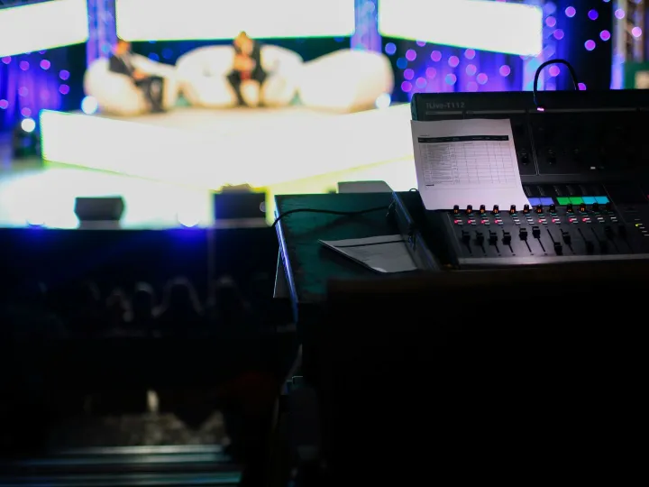 Sound console in a studio setting for a live event with blurred audience view.