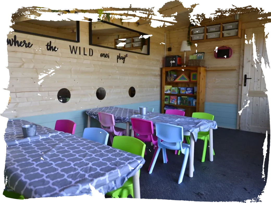The Wild Explorers cabin classroom with low tables, colourful children’s chairs, a bookcase and a Where the Wild Ones Play sign