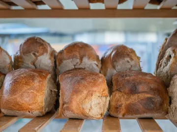 Close-up of rustic, crusty loaf bread displayed on a wooden shelf.